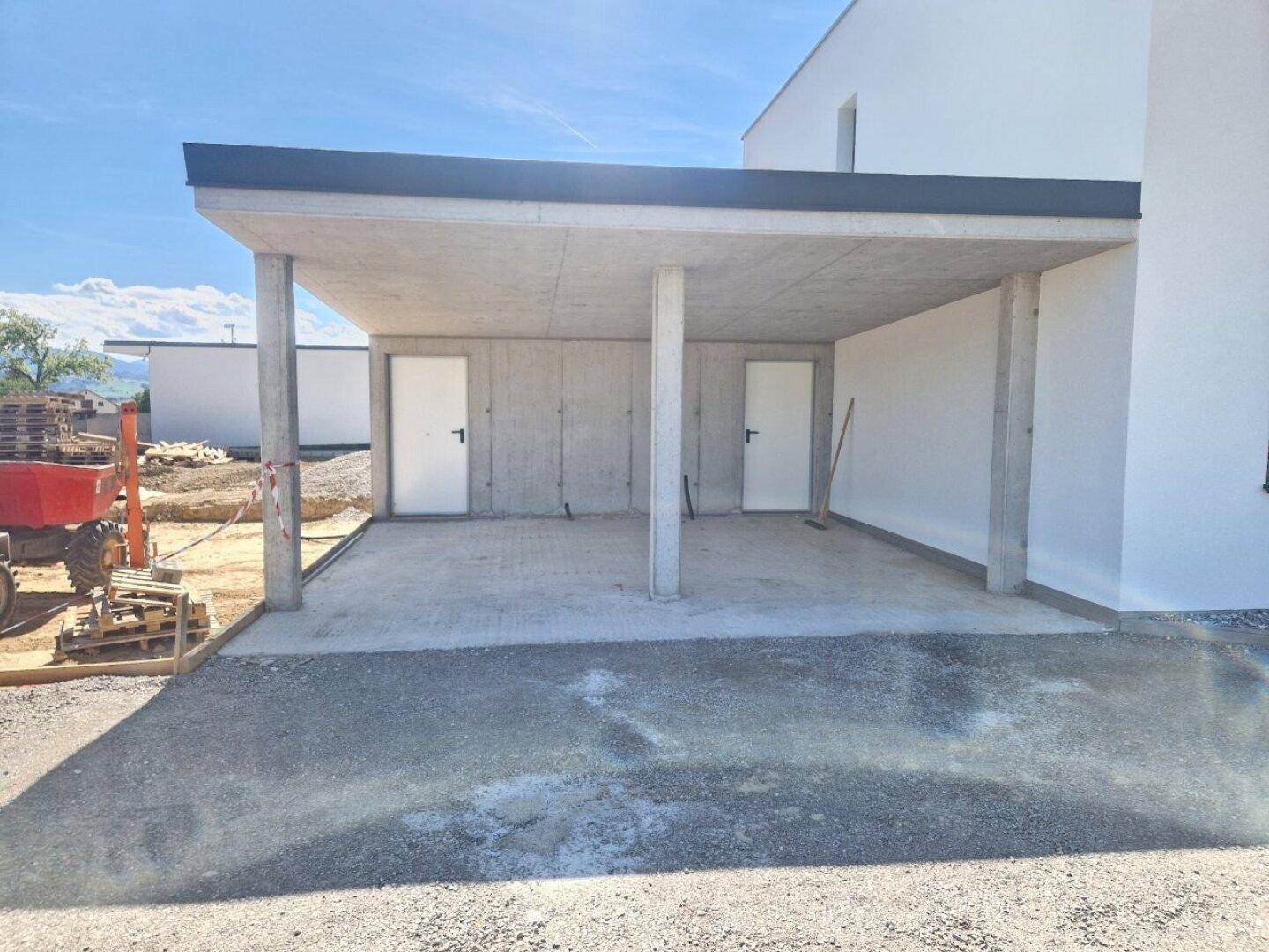 Überdachter Carport-Bereich im Rohbau mit Betonstützen und zwei Türen zu Abstellräumen.