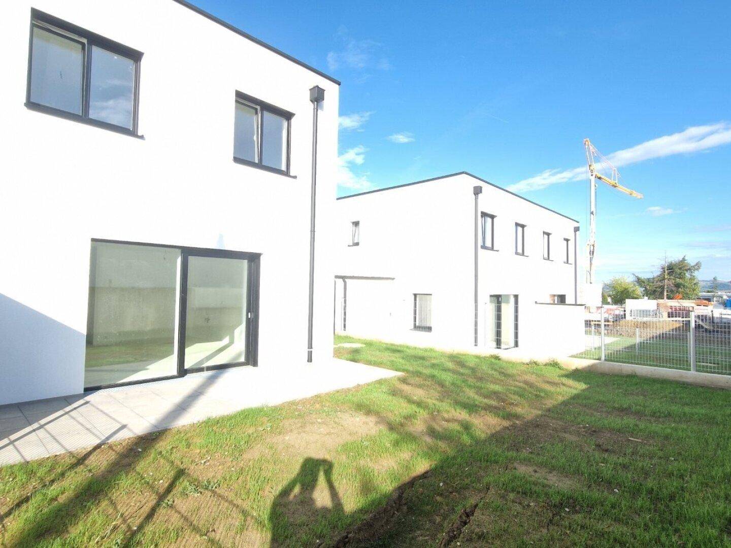 Zwei moderne, weiße Neubauten mit großen Fenstern und Terrassenbereichen unter blauem Himmel.