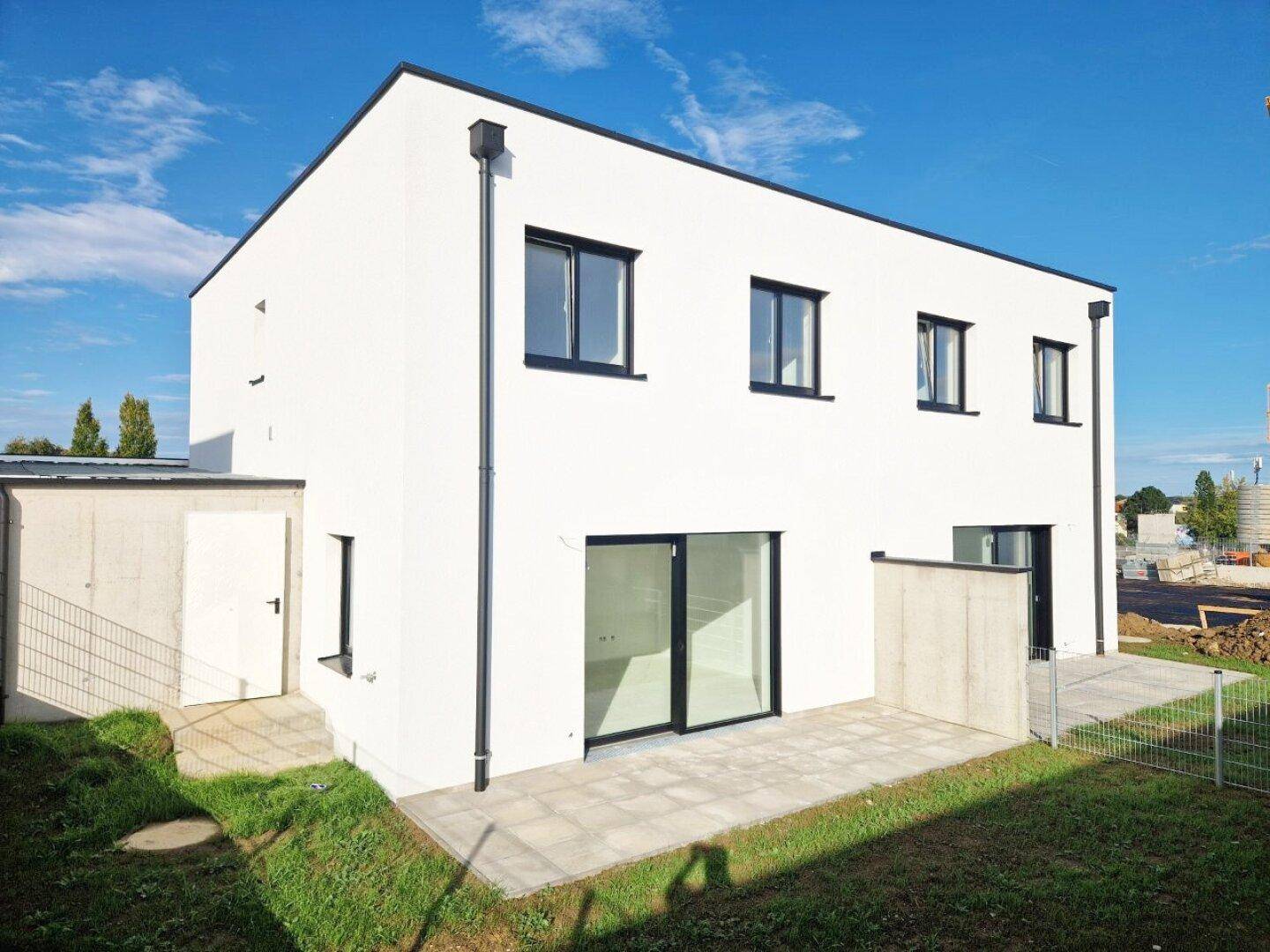 Moderner weißer Neubau mit Flachdach, großer Terrasse und angrenzendem Abstellraum.