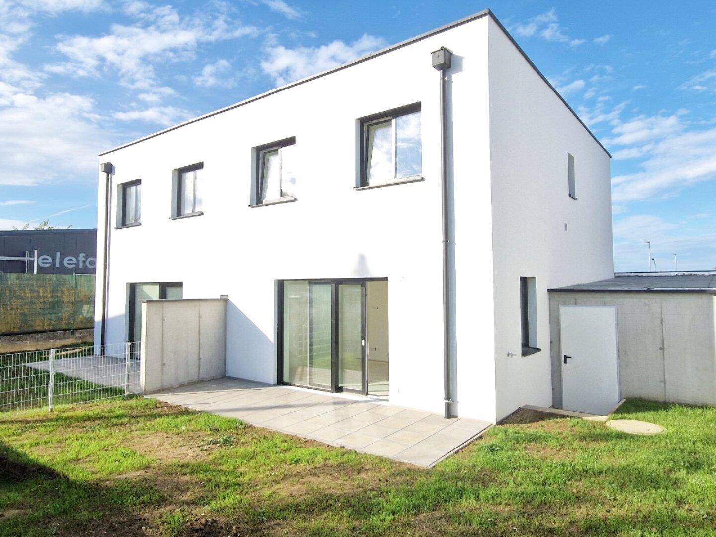 Moderner Neubau mit weißer Fassade, großzügiger Terrasse und angrenzendem Abstellbereich im Freien.