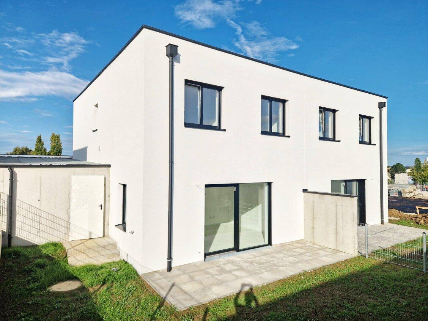 Moderner weißer Neubau mit Flachdach, großer Terrasse und angrenzendem Abstellraum.
