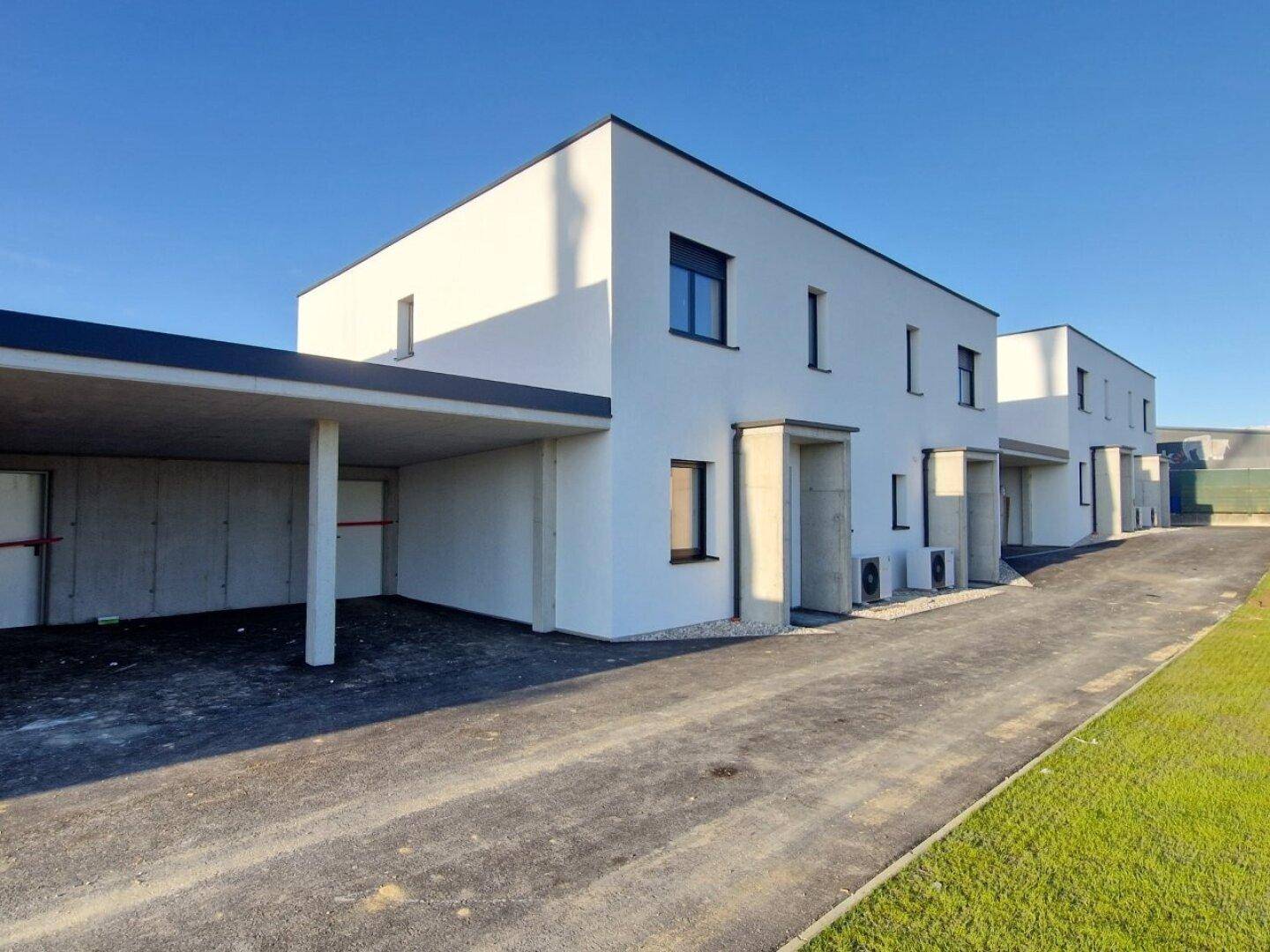 Reihe moderner Häuser mit weißer Fassade, Carport und asphaltierter Zufahrt.