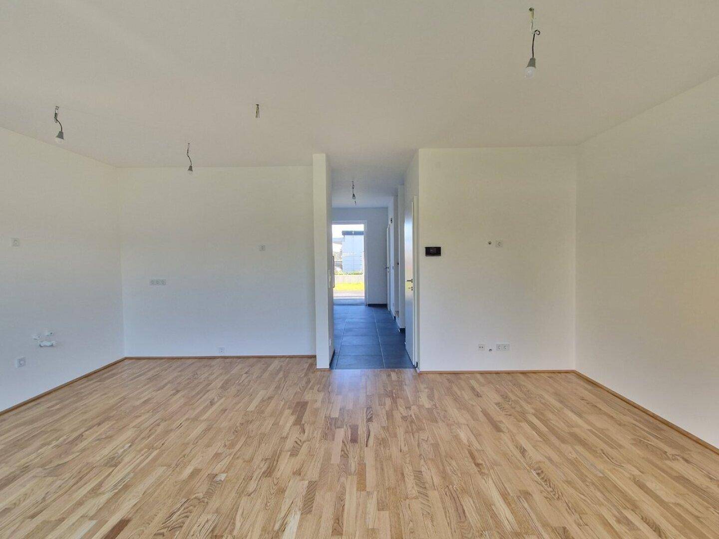 Geräumiges Wohnzimmer mit Holzboden und Blick in den Eingangsbereich.