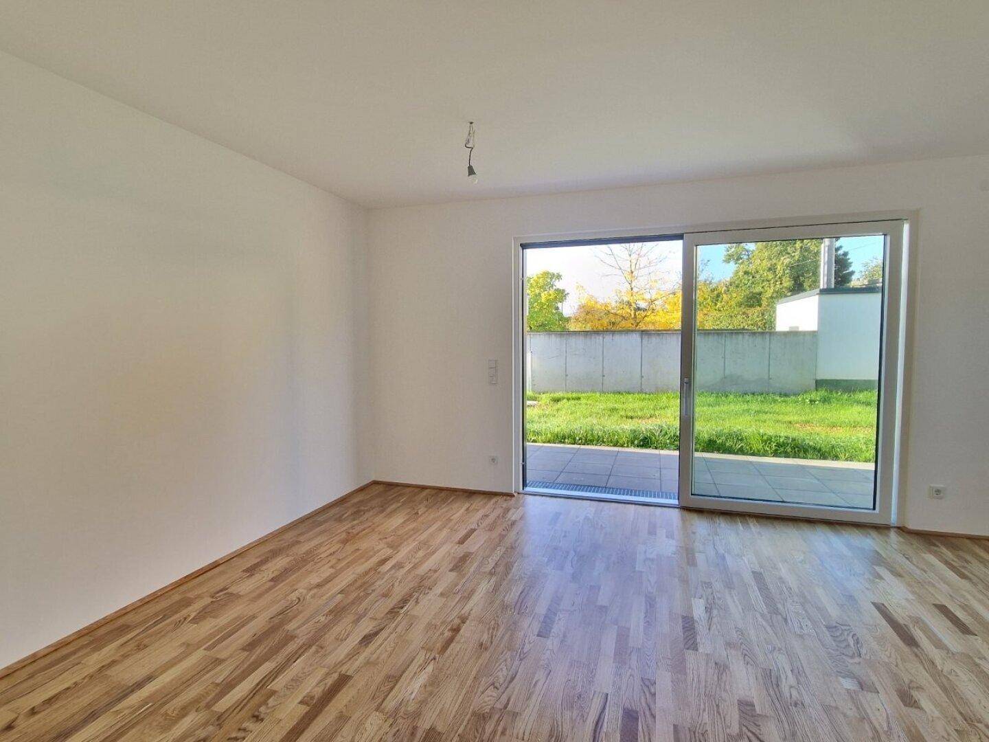 Lichtdurchfluteter Raum mit Holzboden und Zugang zu einer Terrasse oder Gartenfläche.