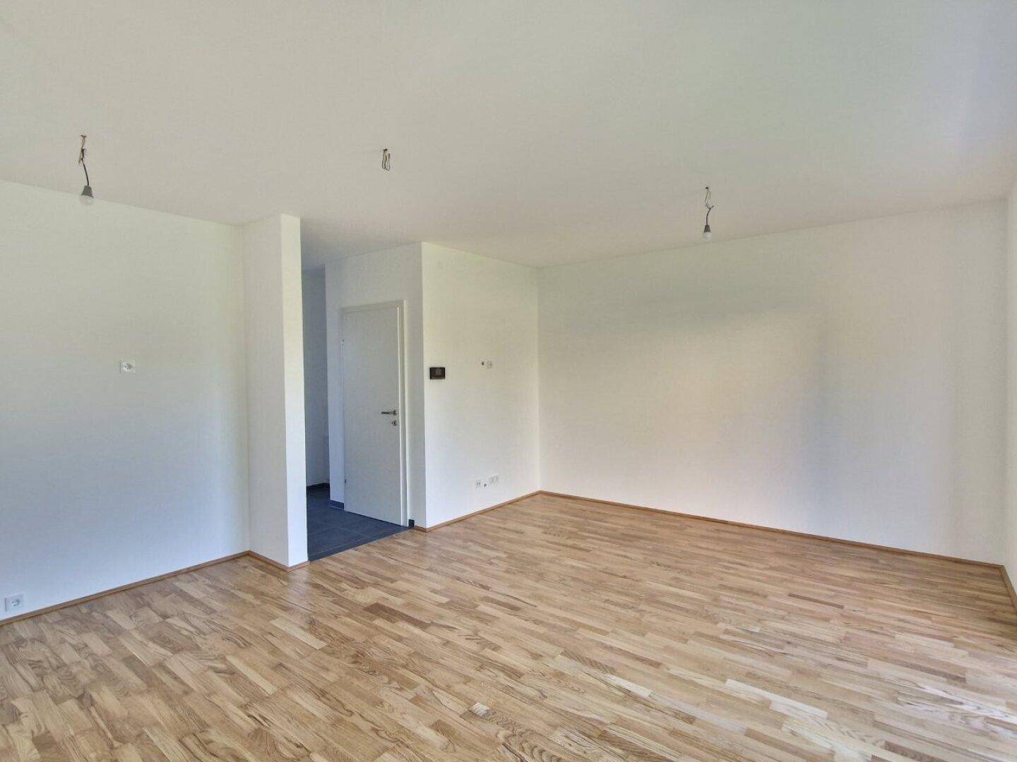 Heller Wohnbereich mit Holzboden und weiß gestrichenen Wänden, bereit zur Einrichtung.