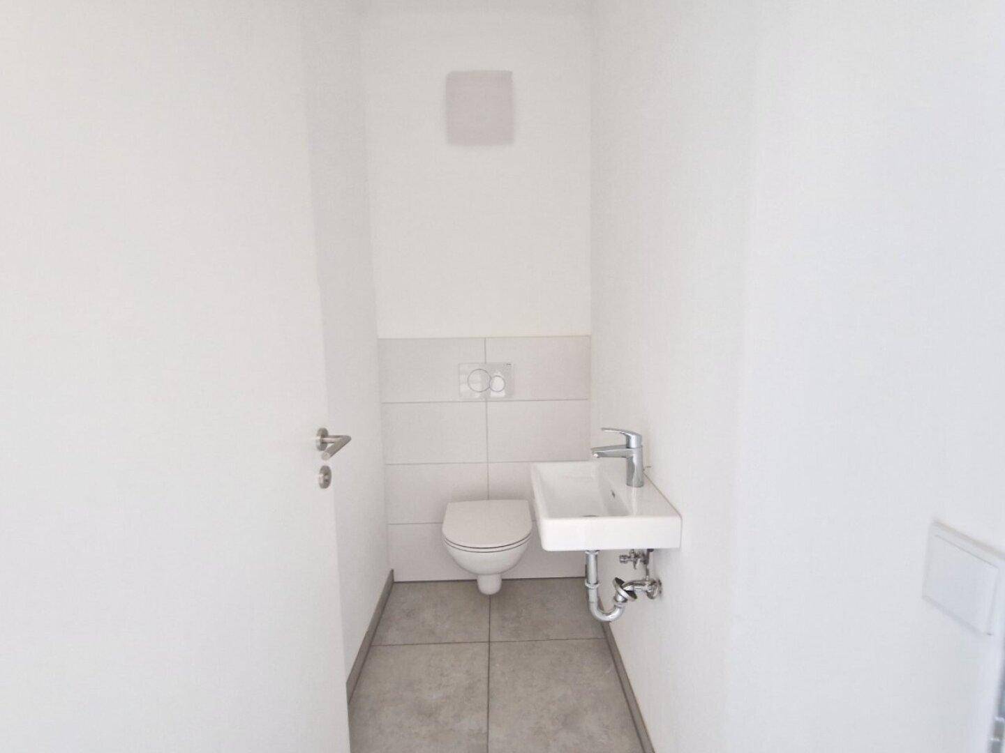 Modernes Gäste-WC mit wandhängendem WC, kleinem Waschbecken und Fliesenboden.