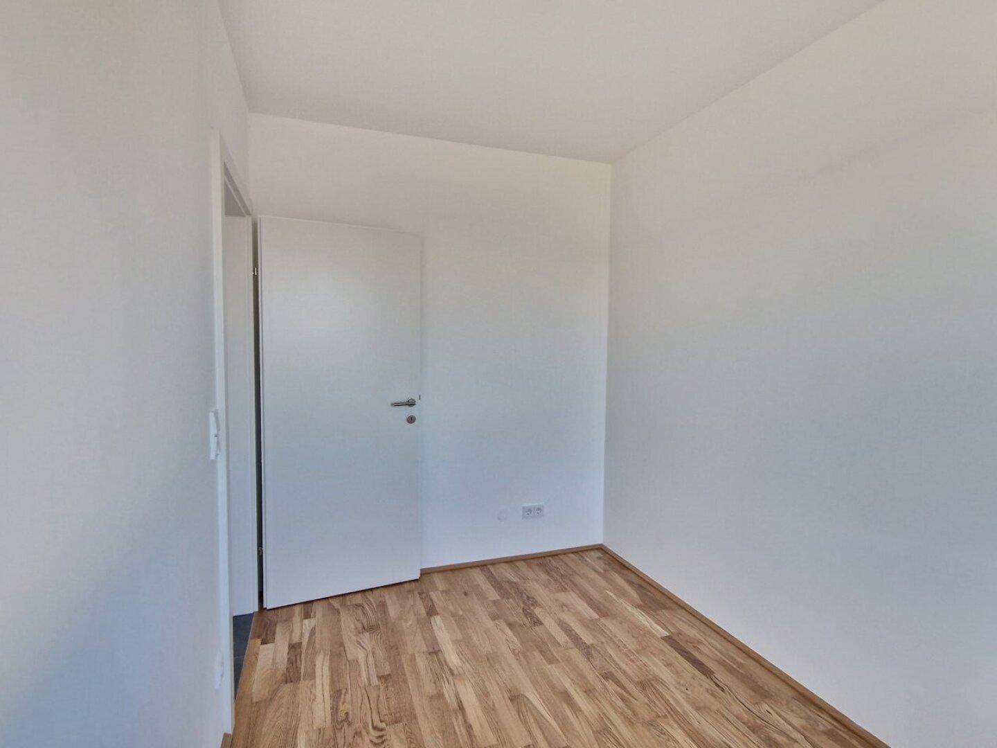 Unmöbliertes Zimmer mit Holzboden und weißer Tür, bereit für individuelle Gestaltung.