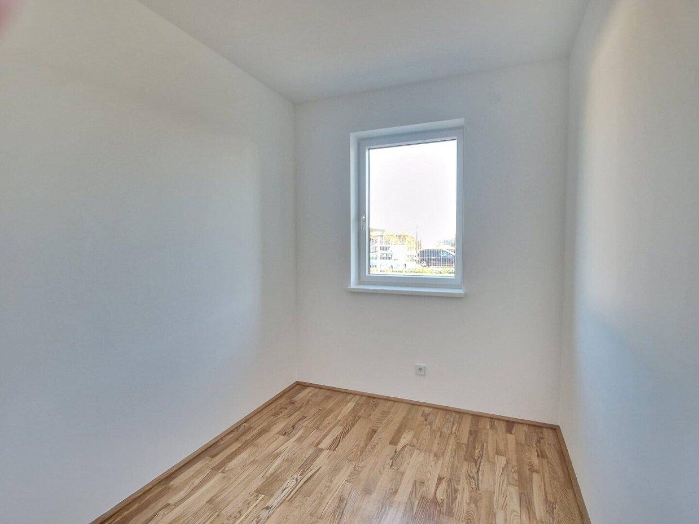 Kleines, helles Zimmer mit Holzboden und einem Fenster, ideal als Kinder- oder Arbeitszimmer.