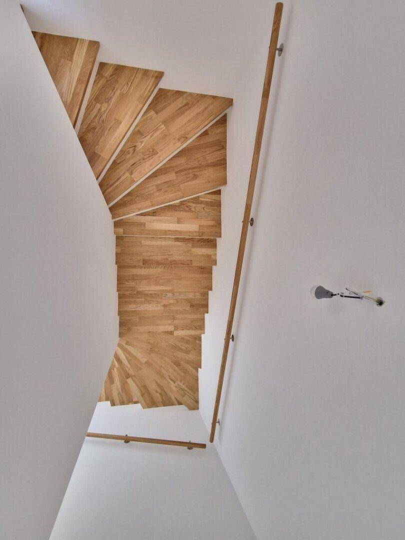 Wendeltreppe mit Holzstufen und minimalistischem Geländer, verbindet die Stockwerke.
