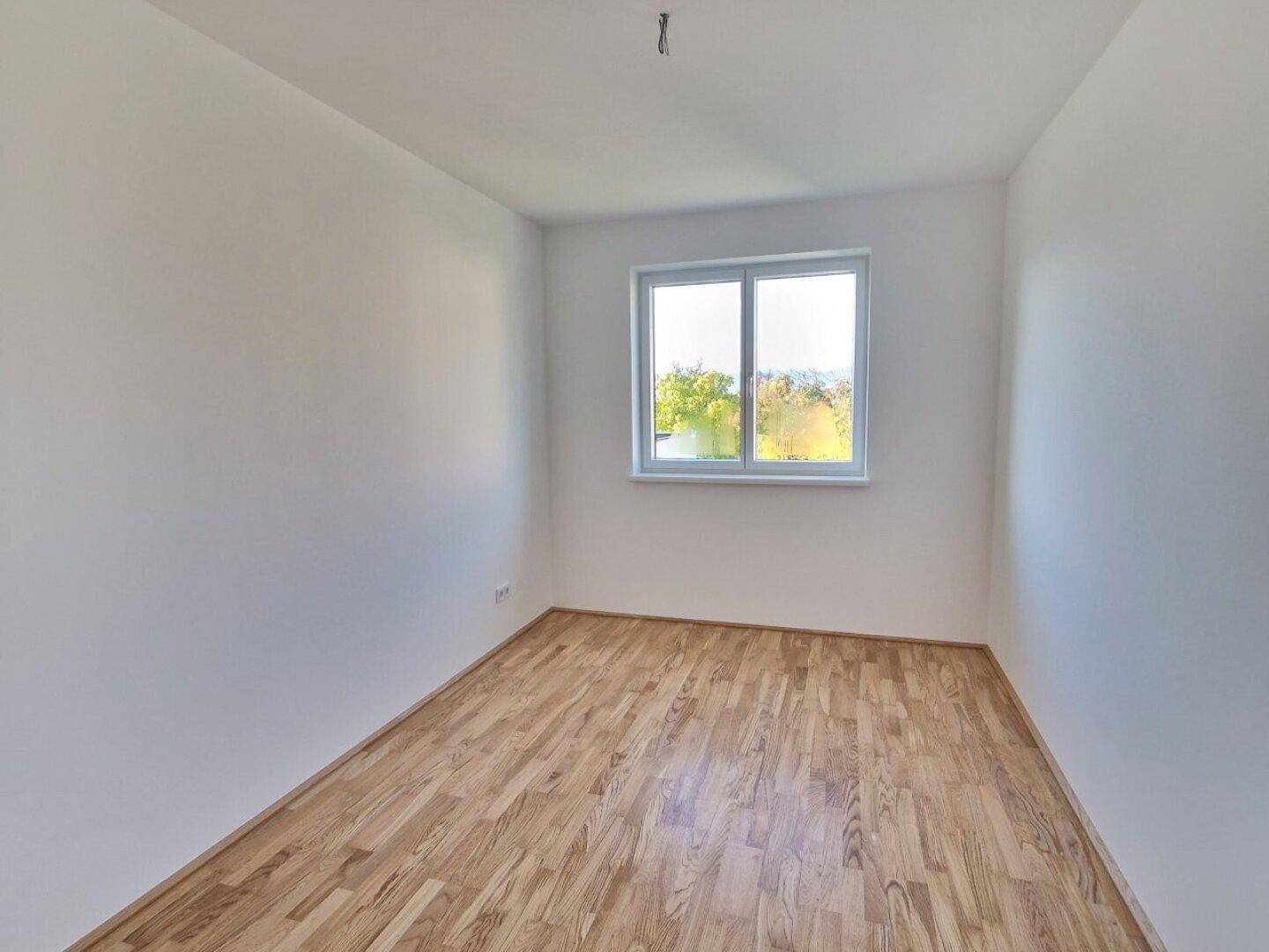 Helles Schlafzimmer mit Holzboden und großem Fenster, bietet viel Tageslicht.