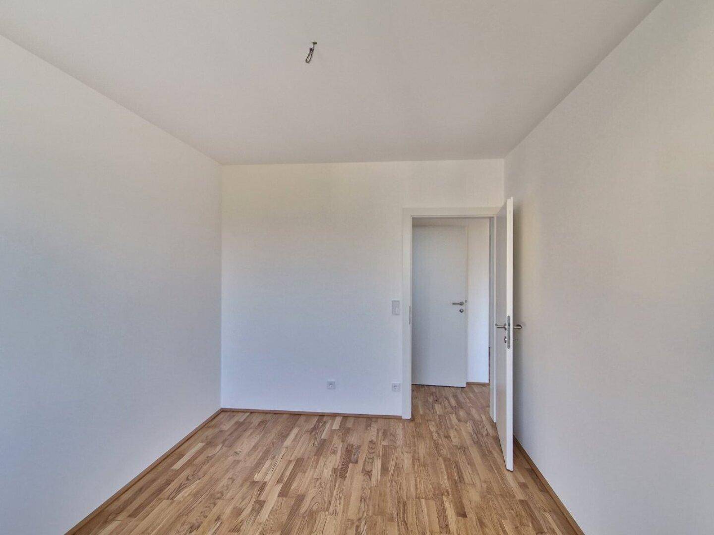 Geräumiges Schlafzimmer mit Holzboden und weißer Tür, bereit zur individuellen Gestaltung.