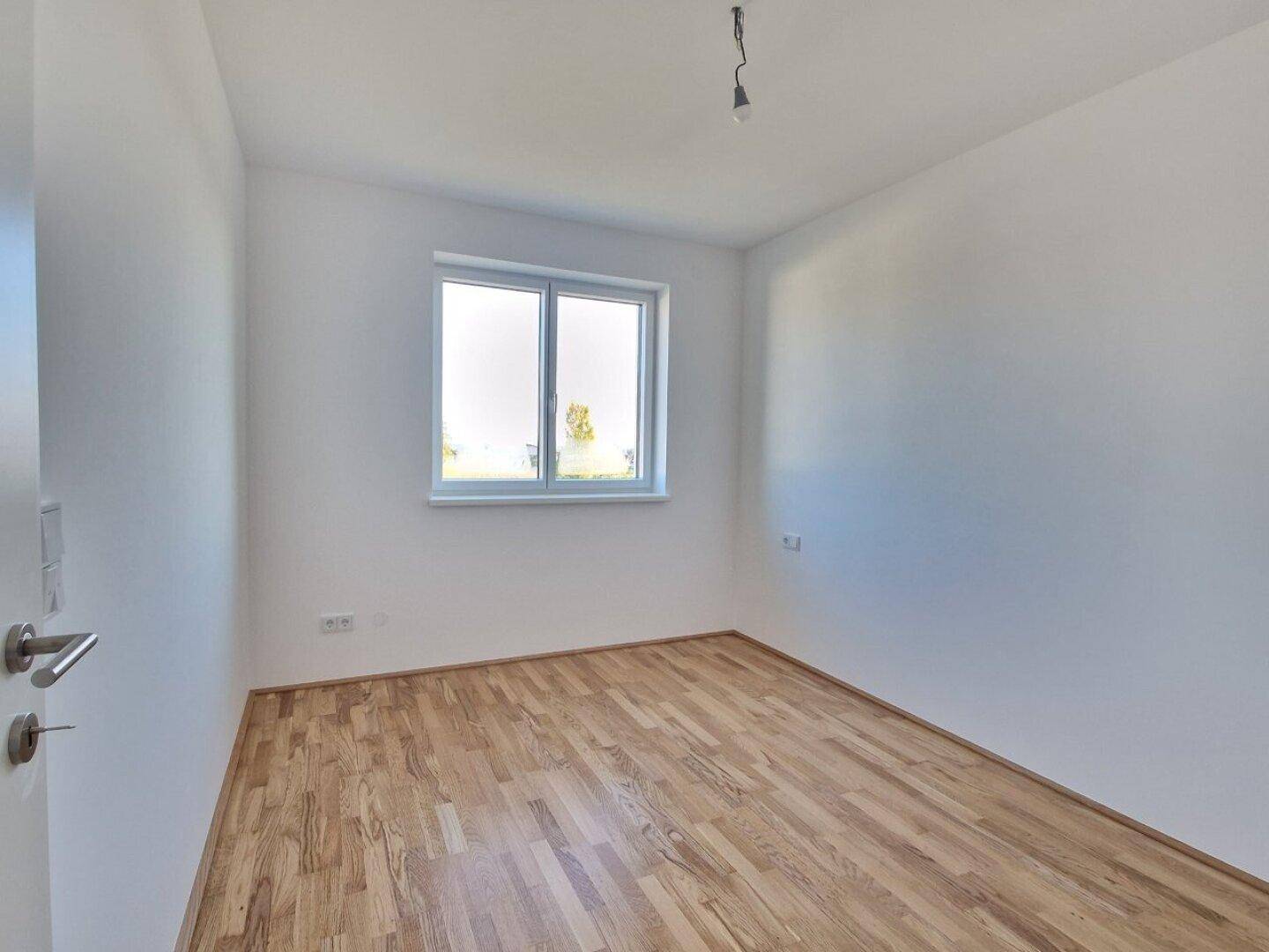 Freundliches Zimmer mit Holzboden und Fenster, ideal als Kinder- oder Gästezimmer.