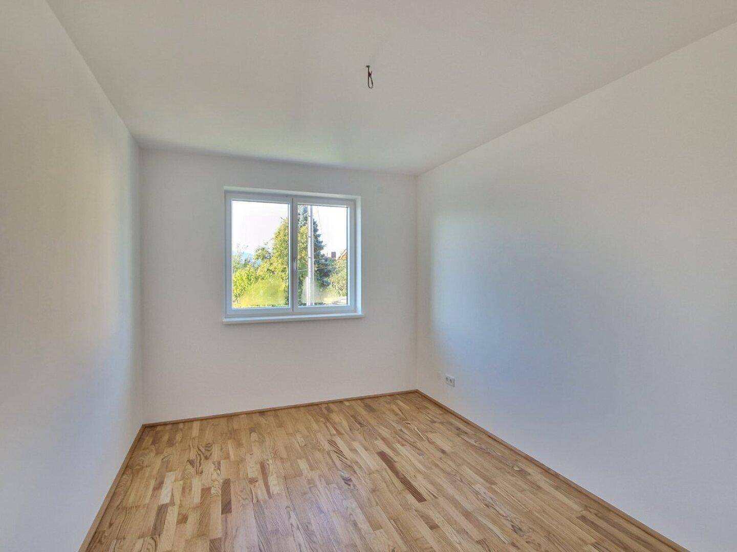 Helles Zimmer mit Holzboden und Blick ins Grüne, ideal für Ruhe und Entspannung.