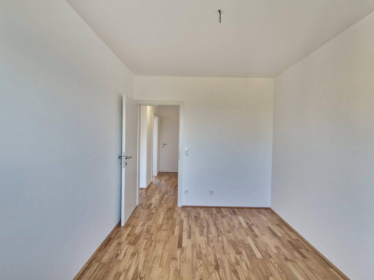 Unmöbliertes Zimmer mit Holzboden und Zugang zu einem Flur, bietet vielseitige Nutzungsmöglichkeiten.
