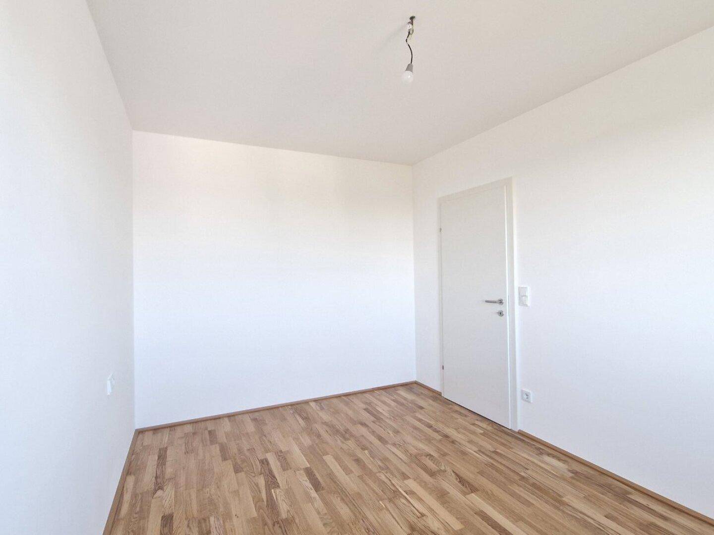 Leeres Zimmer mit Holzboden und weißer Tür, bietet viel Potenzial für persönliche Einrichtung.