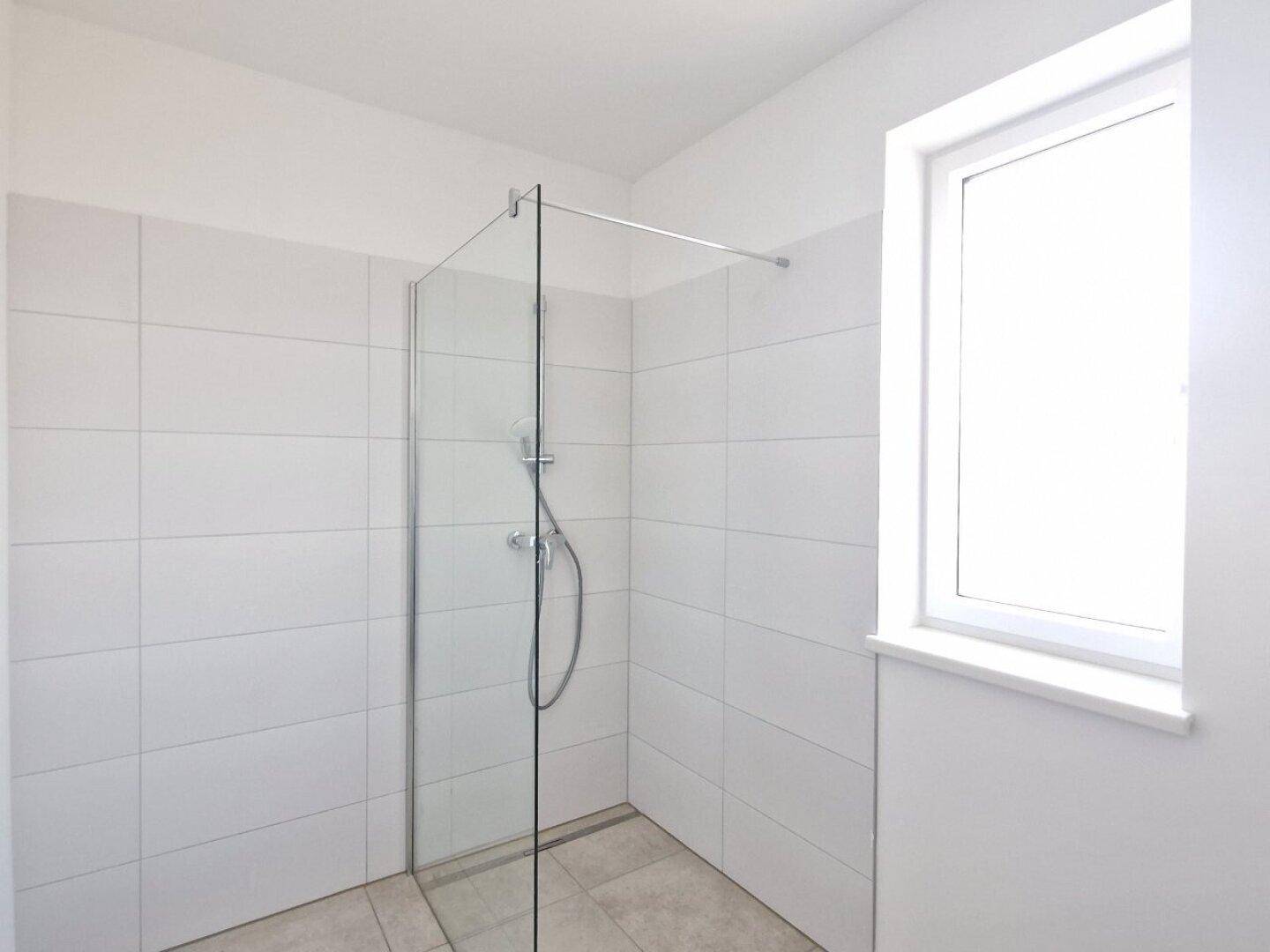Modernes Badezimmer mit ebenerdiger Dusche, Glaswand und Fenster für Tageslicht.