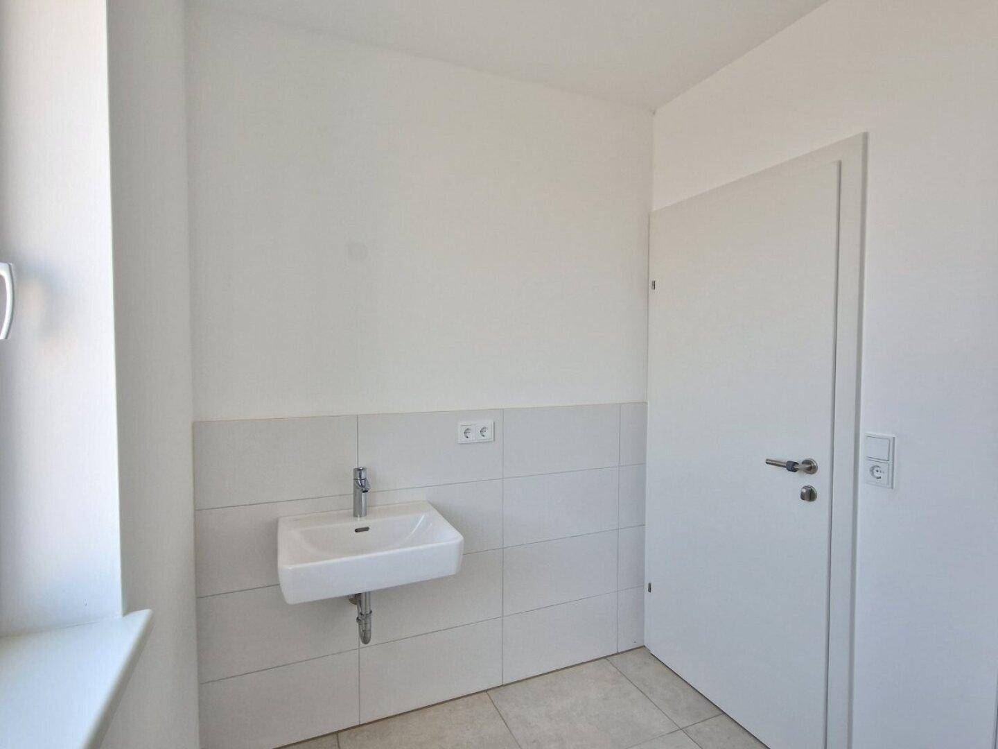 Modernes Badezimmer mit kleinem Waschbecken, Fliesen und weiß gestrichenen Wänden.