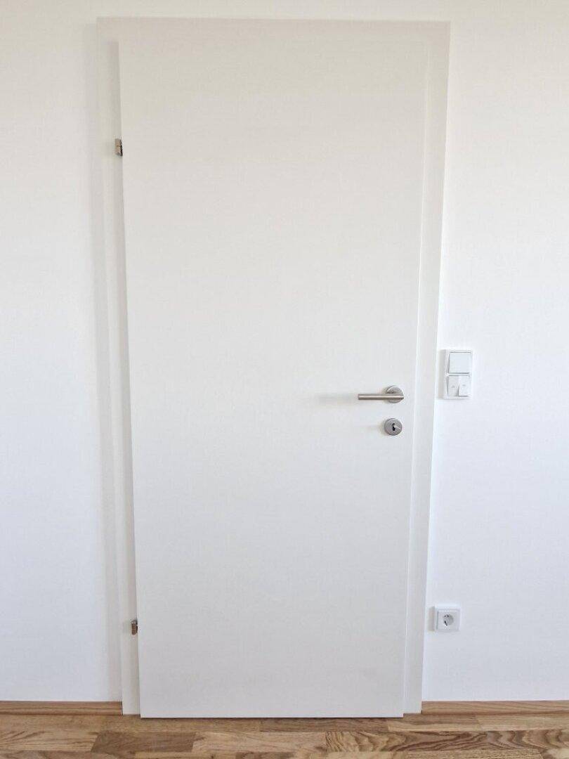 Weiße Innentür mit modernem Griff und Holzboden in einem hellen Raum.