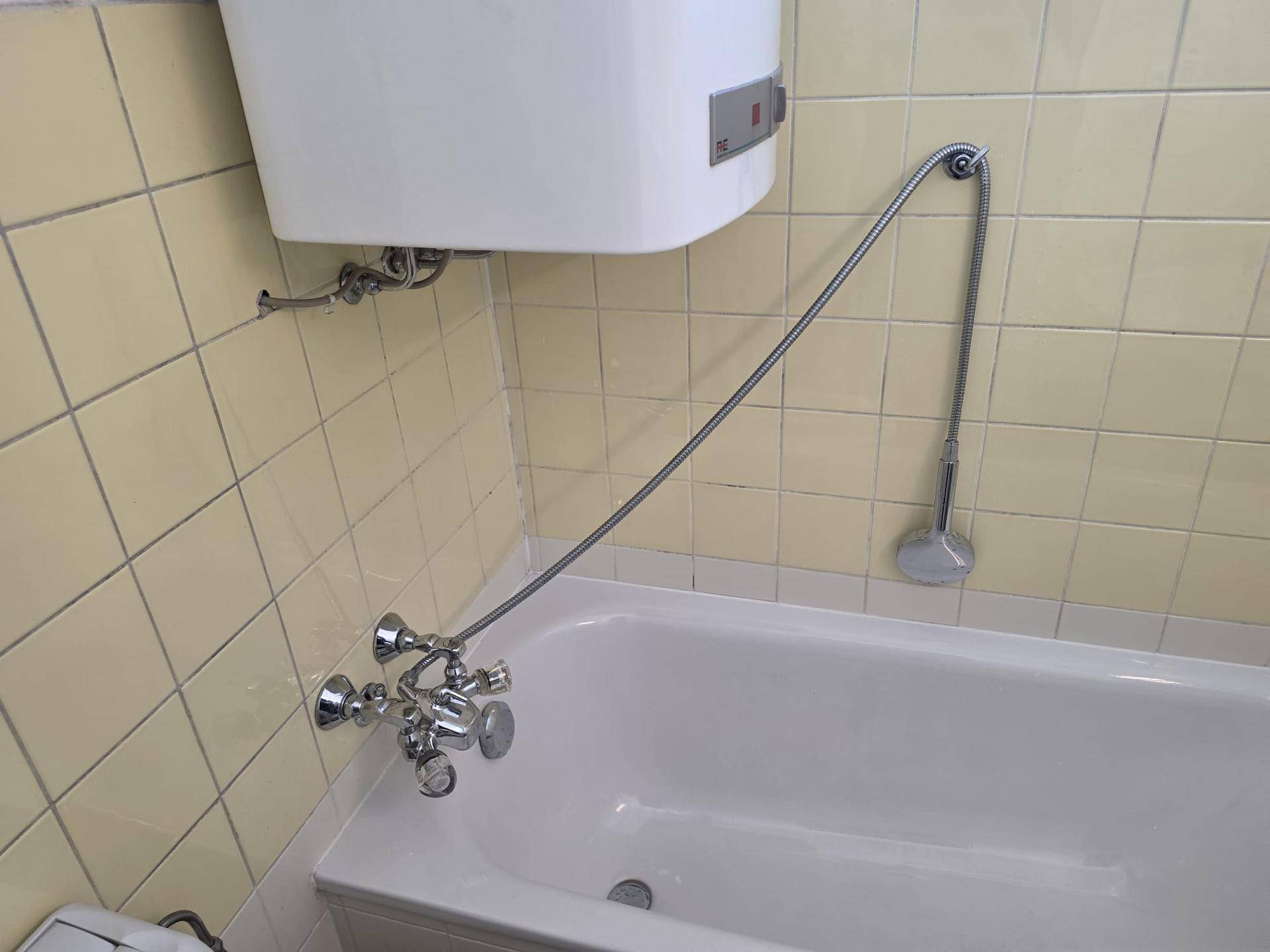 Badezimmer mit Badewanne, gelben Wandfliesen und einem Warmwasserboiler an der Wand.