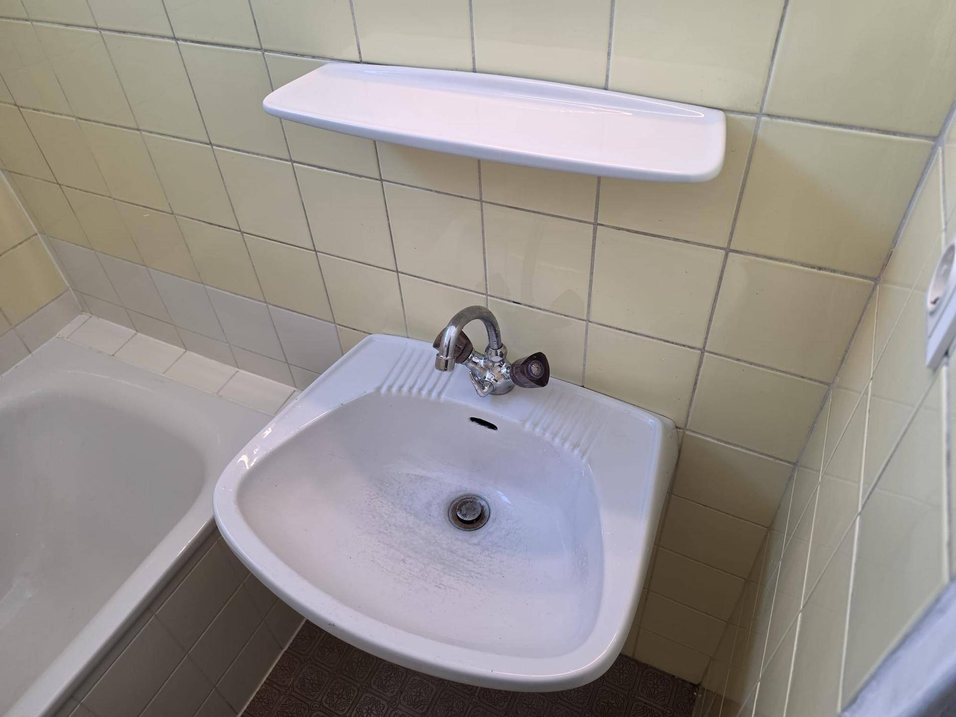 Badezimmer mit einem kleinen Eckwaschbecken, gelben Fliesen und einer Ablagefläche.