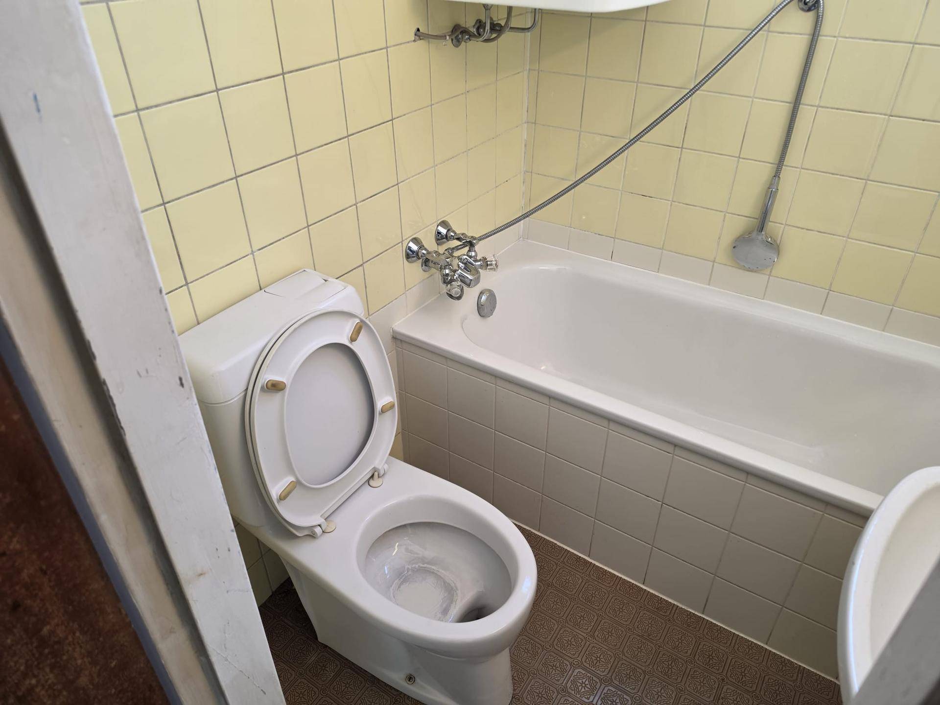 Badezimmer mit Toilette, Badewanne und gelben Fliesen, das eine ältere Ausstattung zeigt.