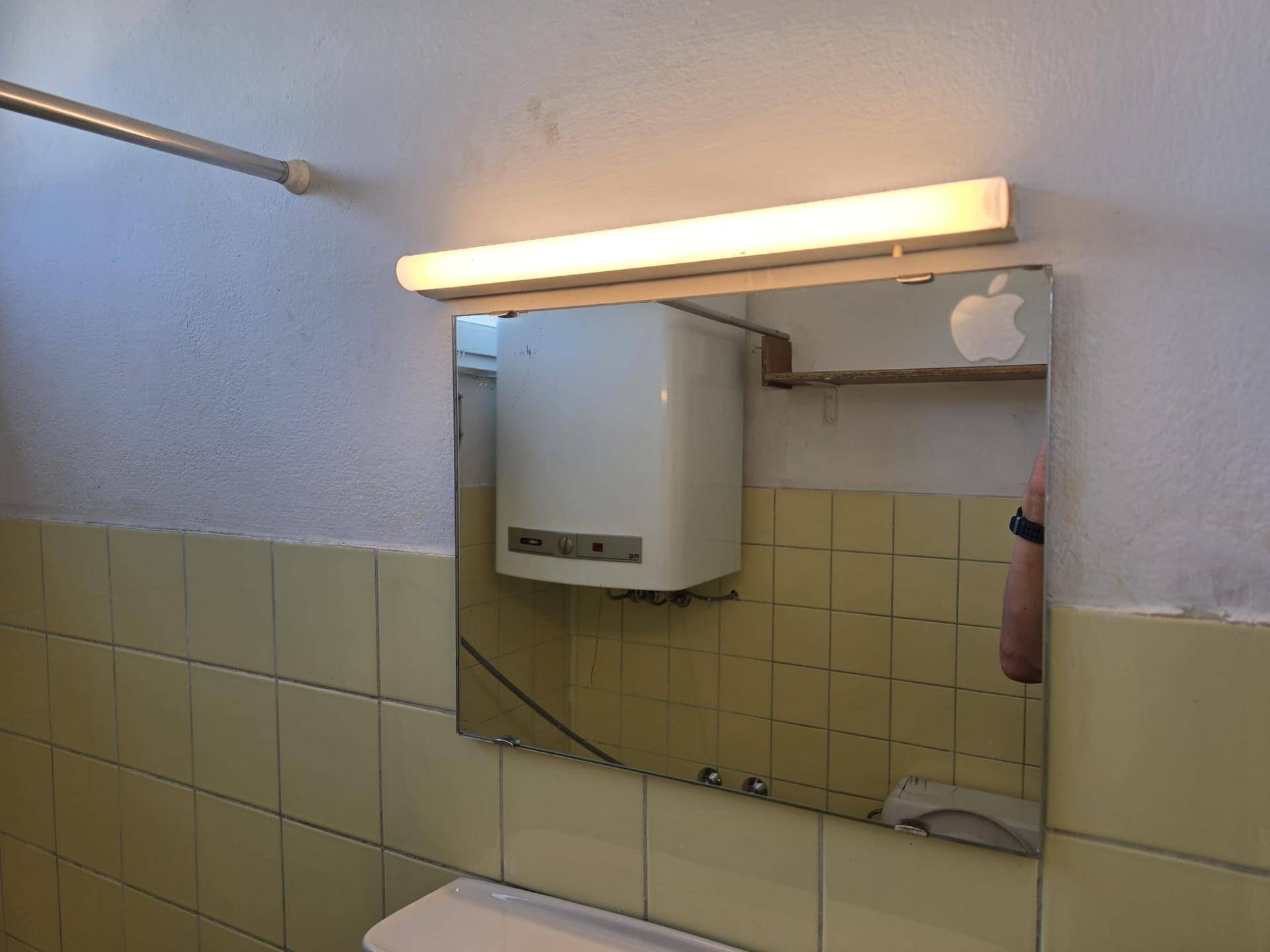 Badezimmer mit gelben Fliesen, einem Spiegel und einem Warmwasserboiler über dem Waschbecken.