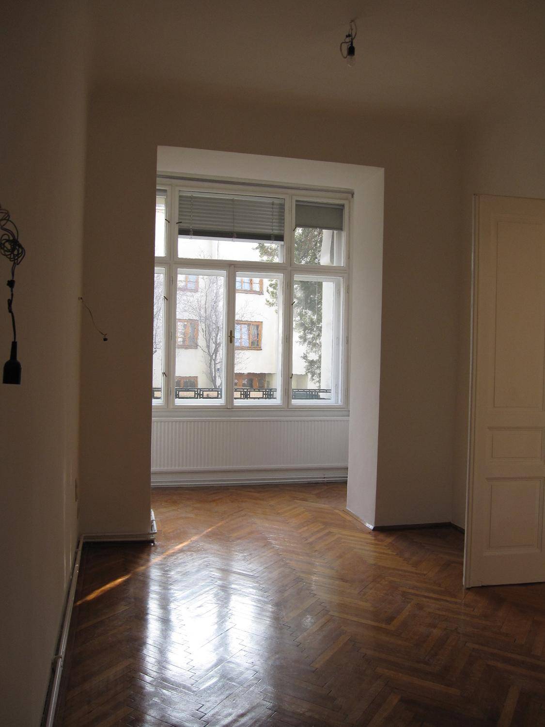 Heller Raum mit glänzendem Fischgrätparkett und großem Fenster, das viel Tageslicht hereinlässt.
