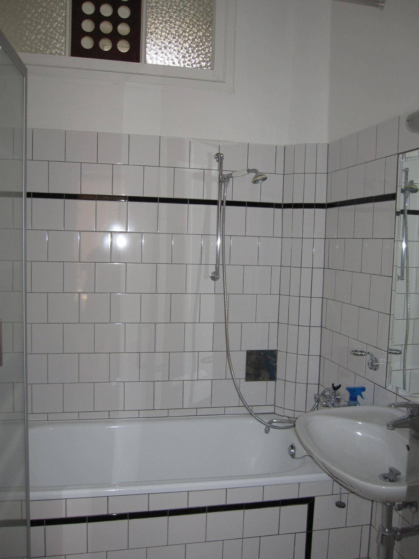 Helles Badezimmer mit weißen Fliesen, Badewanne mit Duschfunktion und einem Waschbecken.