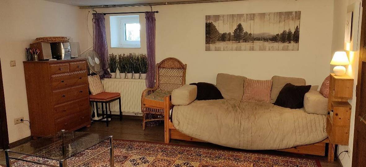 Gemütliches Wohnzimmer mit Sofa, Holzkommode und einem kleinen Fenster, das Tageslicht hereinlässt.