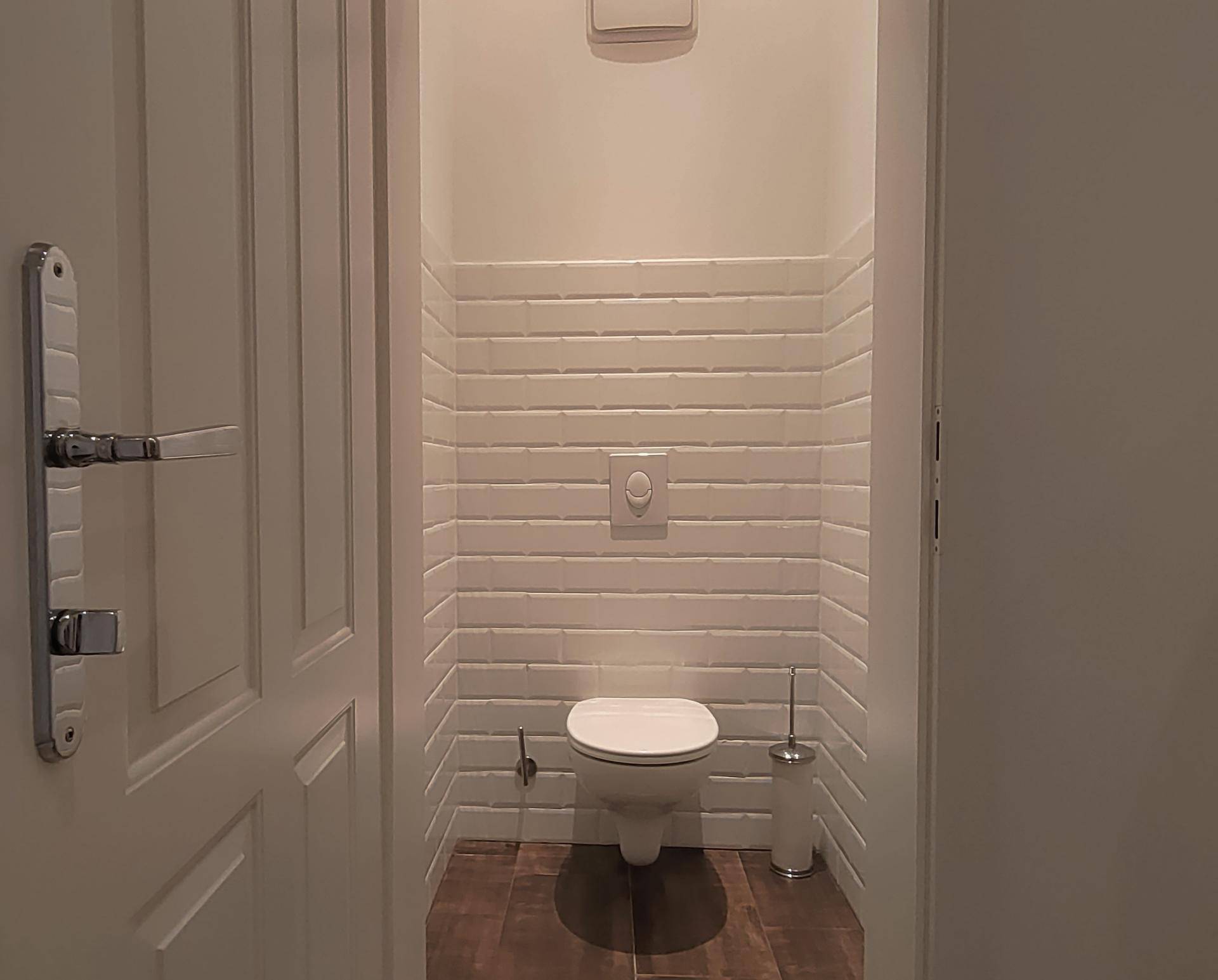 Separate Gästetoilette mit Wand-WC und modernen weißen Wandfliesen.