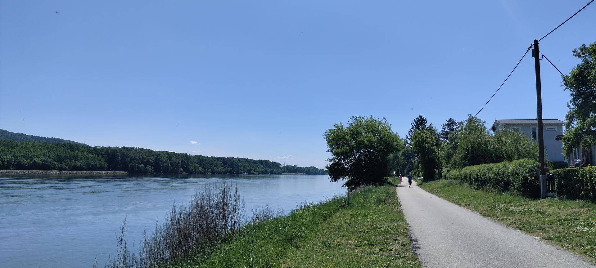 Malerischer Blick auf einen Fluss mit bewaldeten Ufern und einem Spazierweg am Wasser.