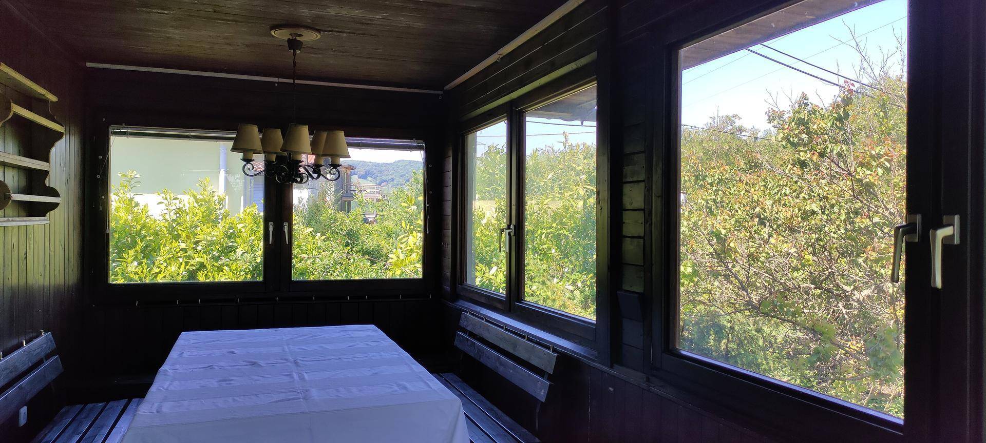 Heller Wintergarten mit großen Fenstern, Holzbänken und einem Esstisch mit Blick ins Grüne.