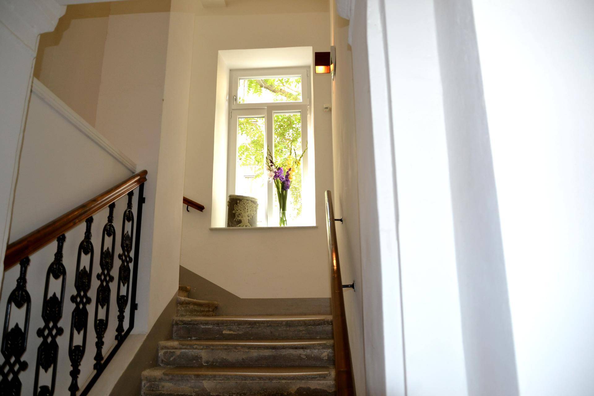 Historisches Treppenhaus mit Holzgeländer, schmiedeeisernen Elementen und Fenster.