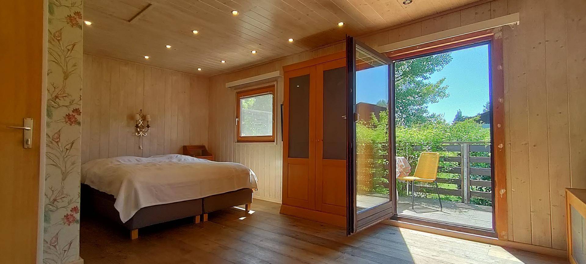 Helles Schlafzimmer mit Holzboden, Holzdecke und direktem Zugang zu einem sonnigen Balkon.