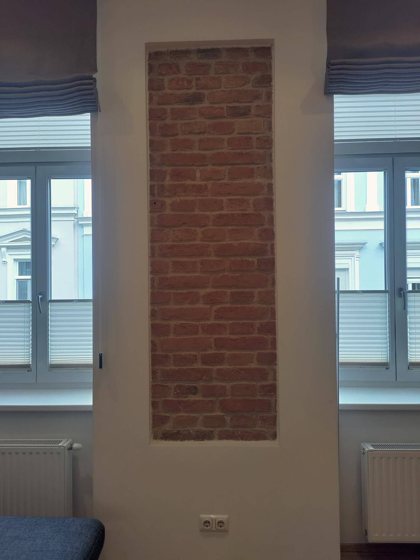 Detailansicht der freigelegten Ziegelwand zwischen zwei Fenstern im Wohnbereich.