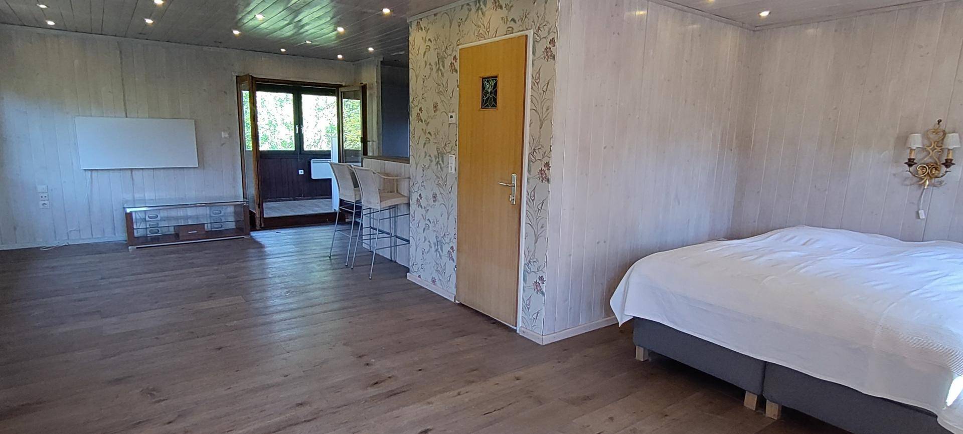 Geräumiger Wohnbereich mit Holzboden, Tapeten und einem Schlafbereich im Hintergrund.