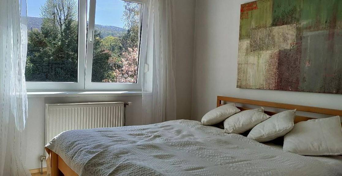 Helles Schlafzimmer mit Doppelbett, weißen Wänden und großem Fenster mit Blick ins Grüne.