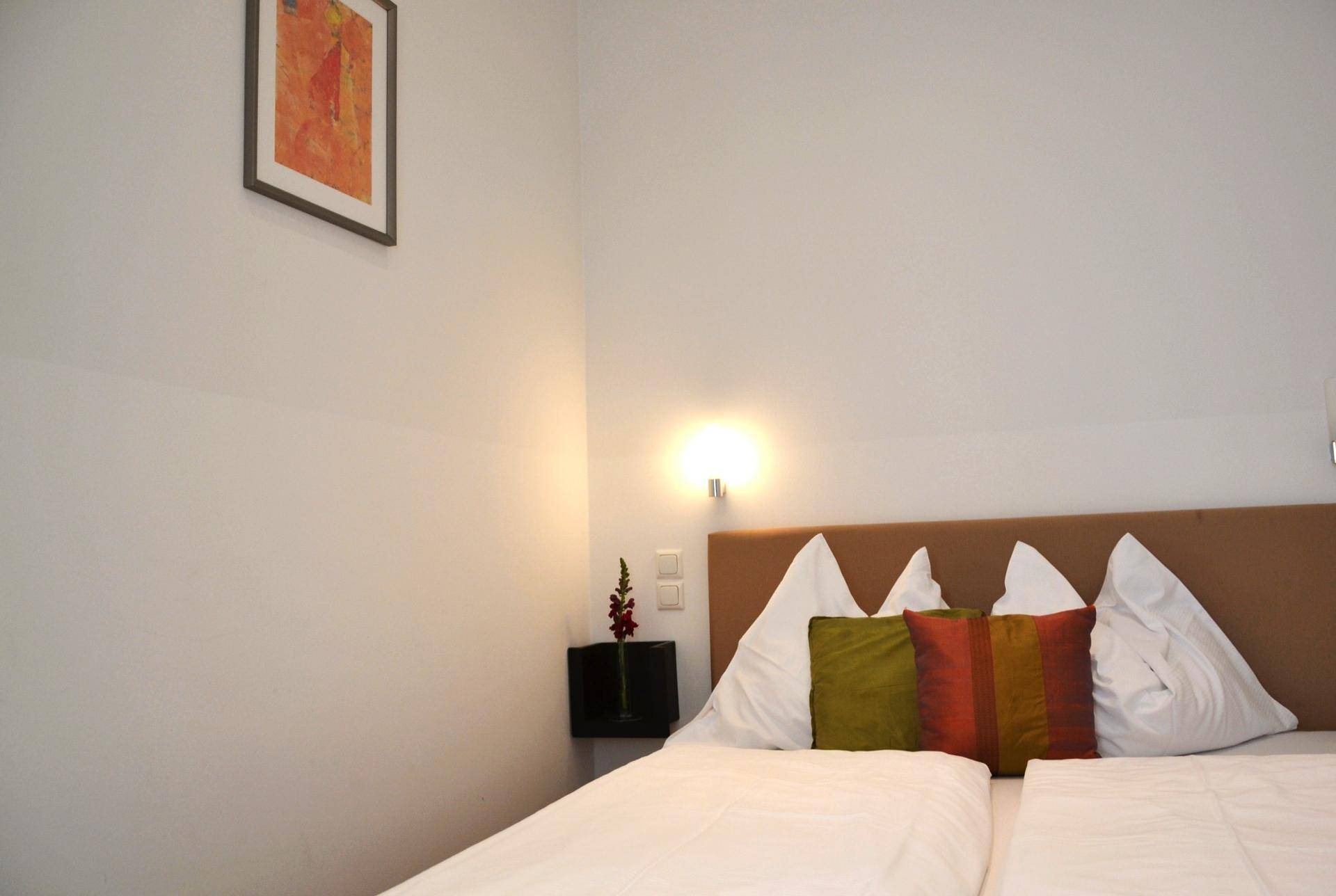 Helles Schlafzimmer mit Doppelbett, Nachttisch und schlichter Wanddekoration.