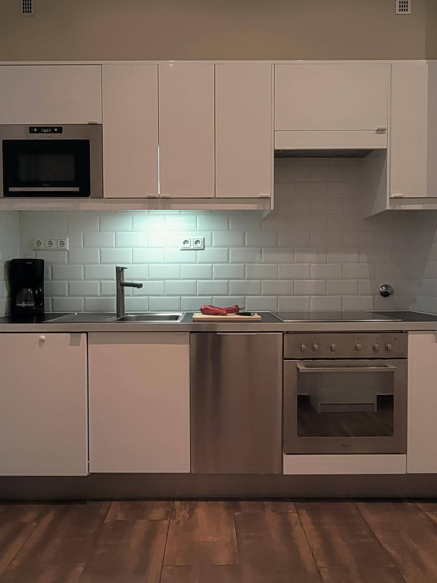 Helle Einbauküche mit weißen Hochglanzfronten, Mikrowelle und Backofen.