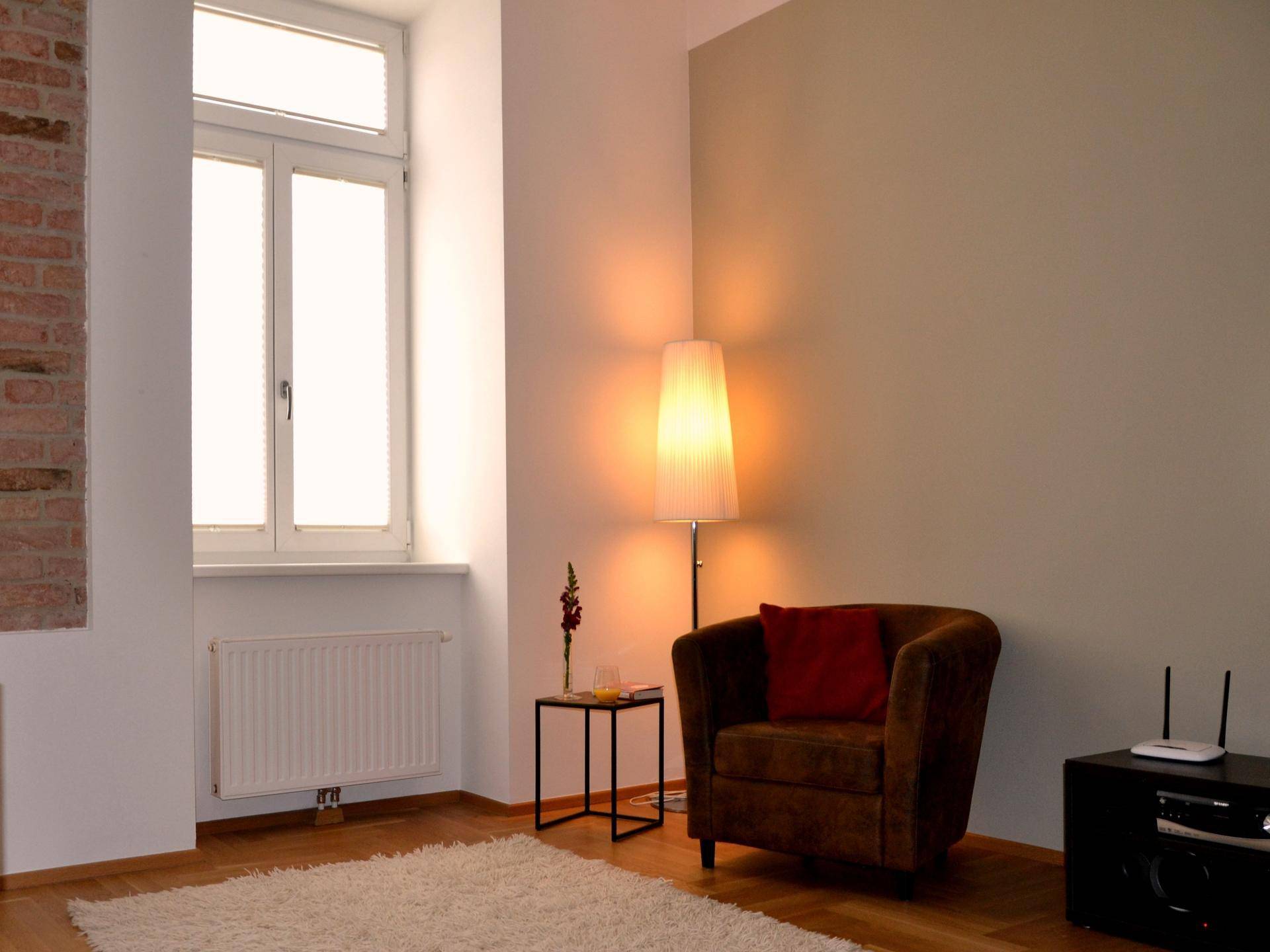 Heller Wohnbereich mit bequemen Sessel, Stehlampe und freigelegter Ziegelwand.