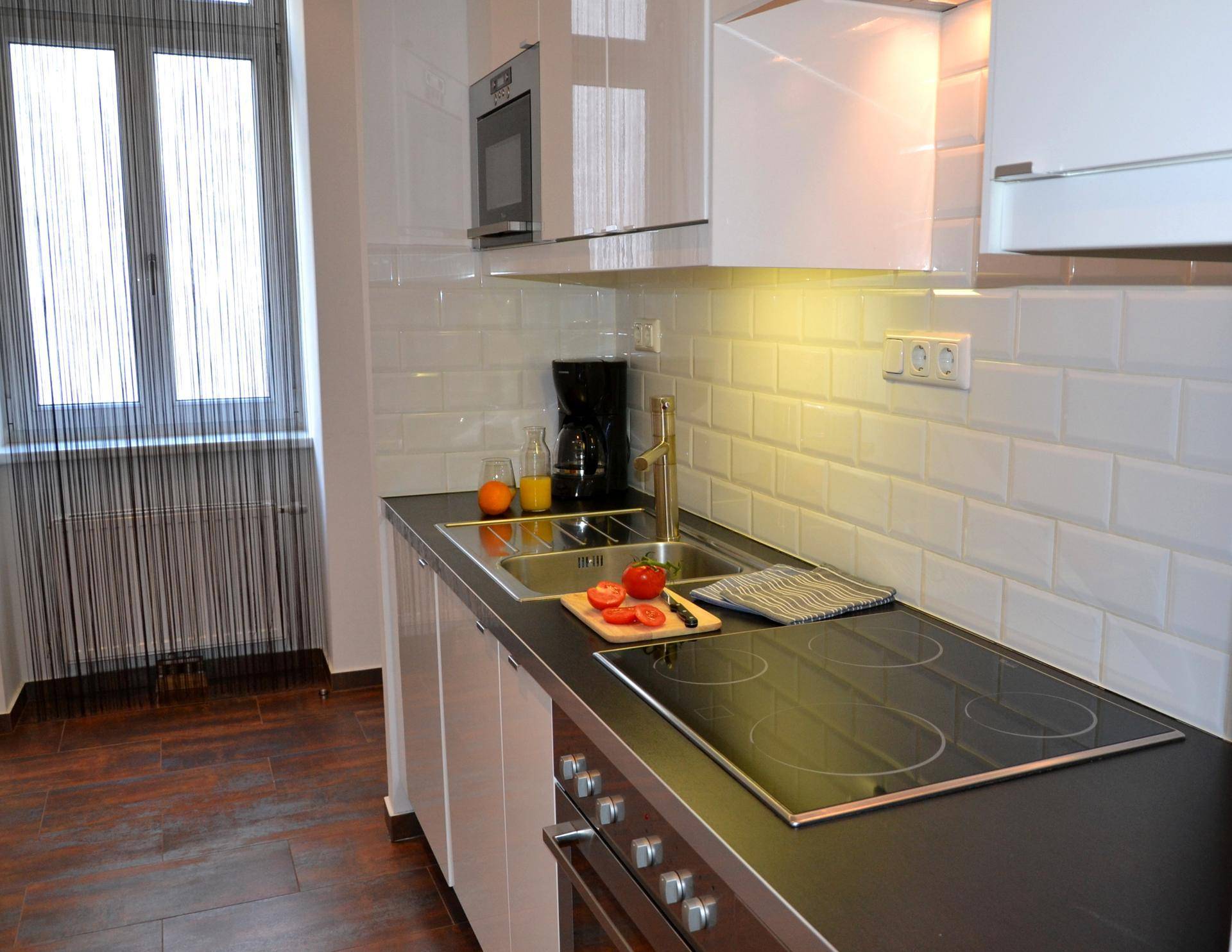 Moderne Küchenzeile mit weißen Hochglanzschränken, Induktionskochfeld und Fenster.
