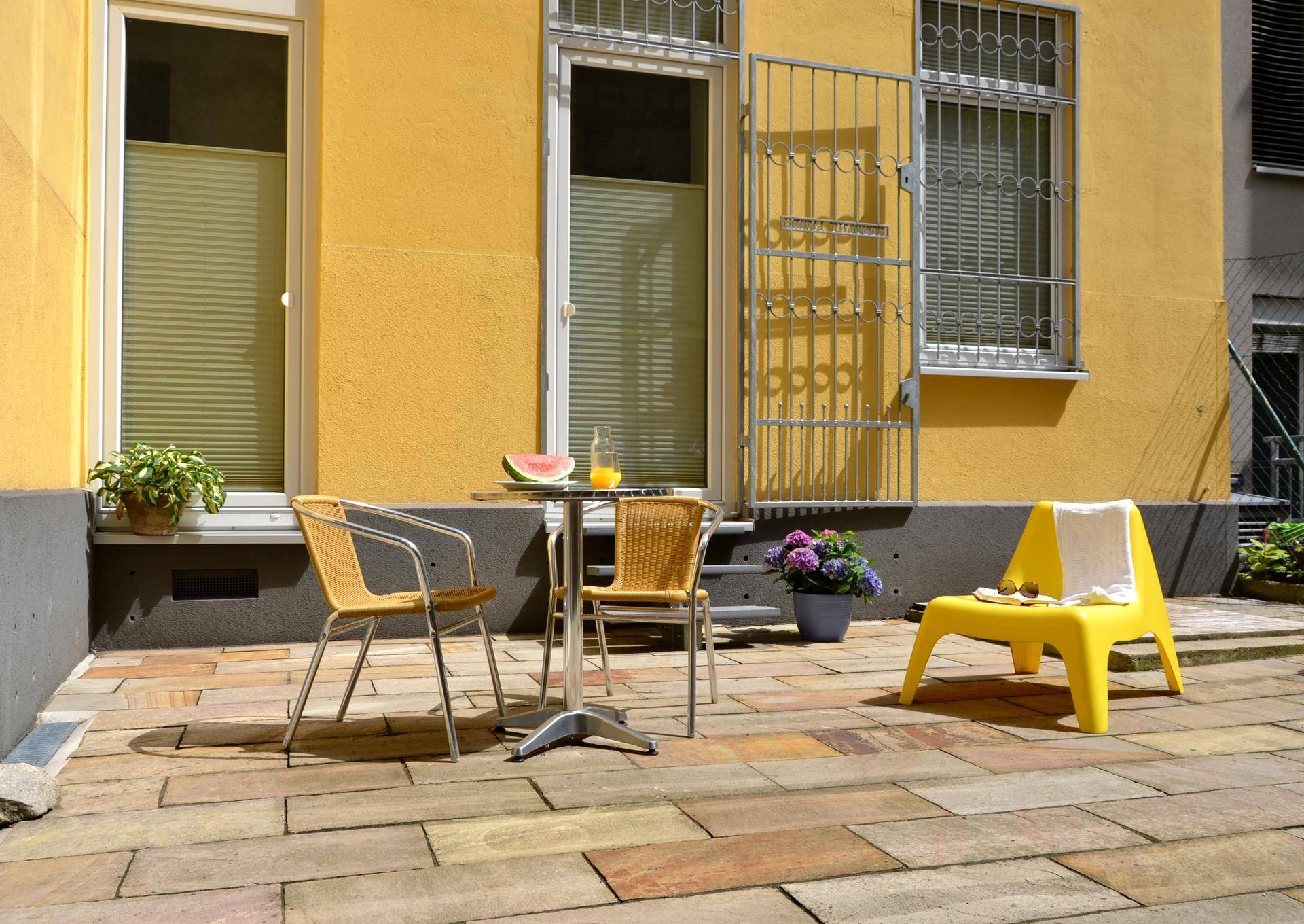 Gemütliche Terrasse mit Sitzgelegenheiten, Steinfliesen und Blick auf die Fassade.