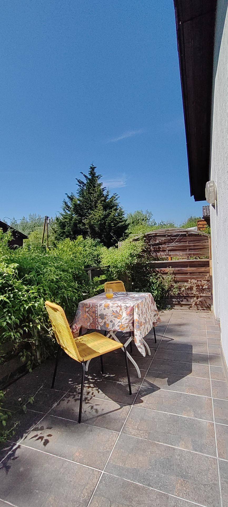 Kleiner, gefliester Terrassenbereich mit Tisch und Stühlen, umgeben von grünen Büschen.