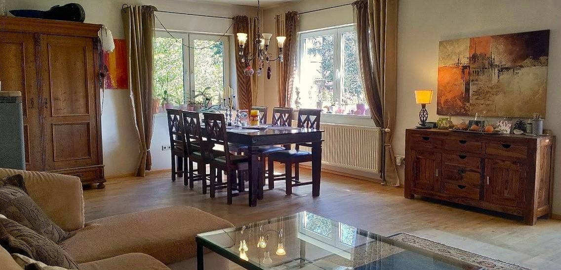 Geräumiger Wohn-Essbereich mit Holzboden, großem Esstisch und gemütlicher Sitzecke, hell durch große Fenster.
