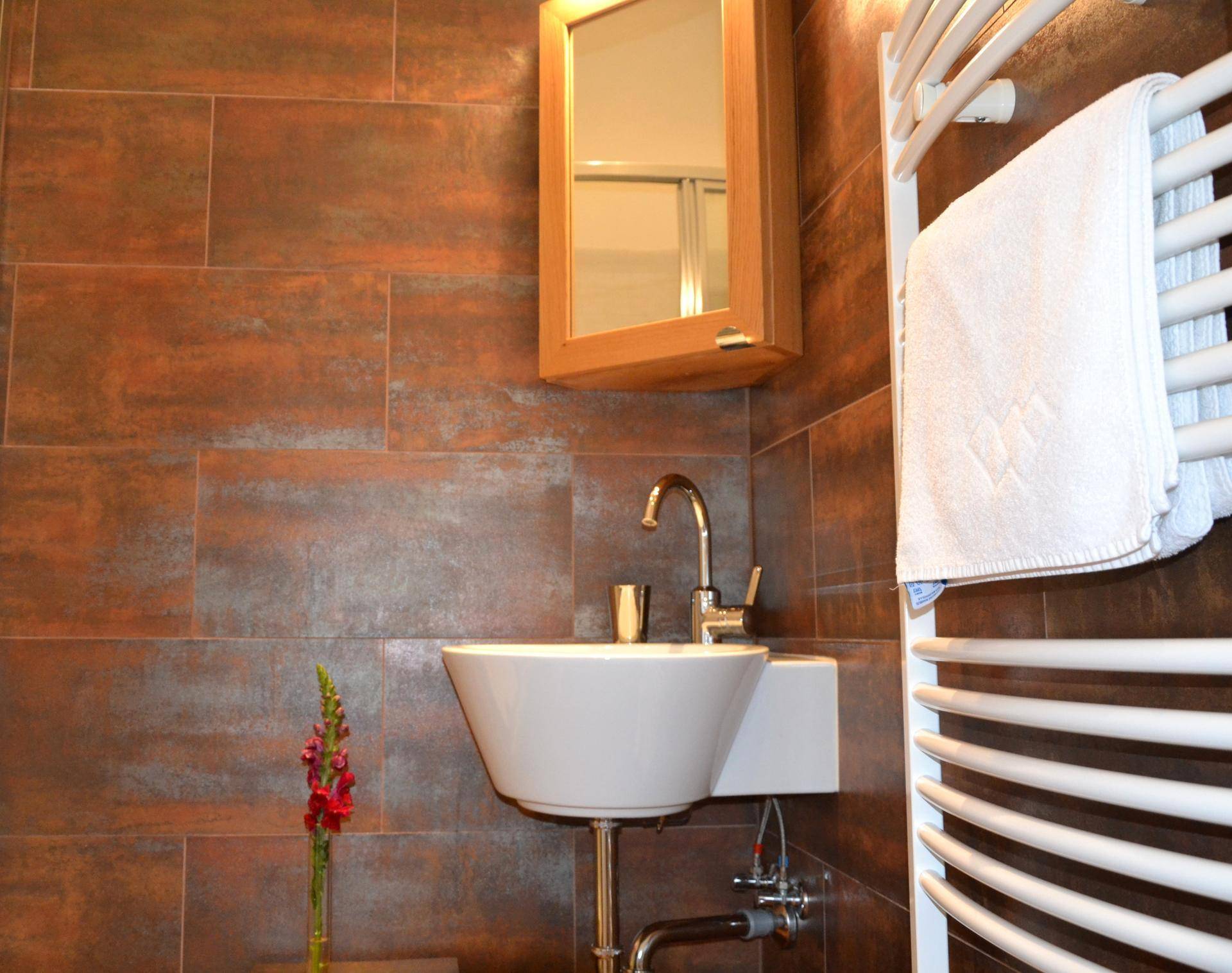 Modernes Badezimmer mit braunen Fliesen, Einzelwaschbecken und beheiztem Handtuchhalter.