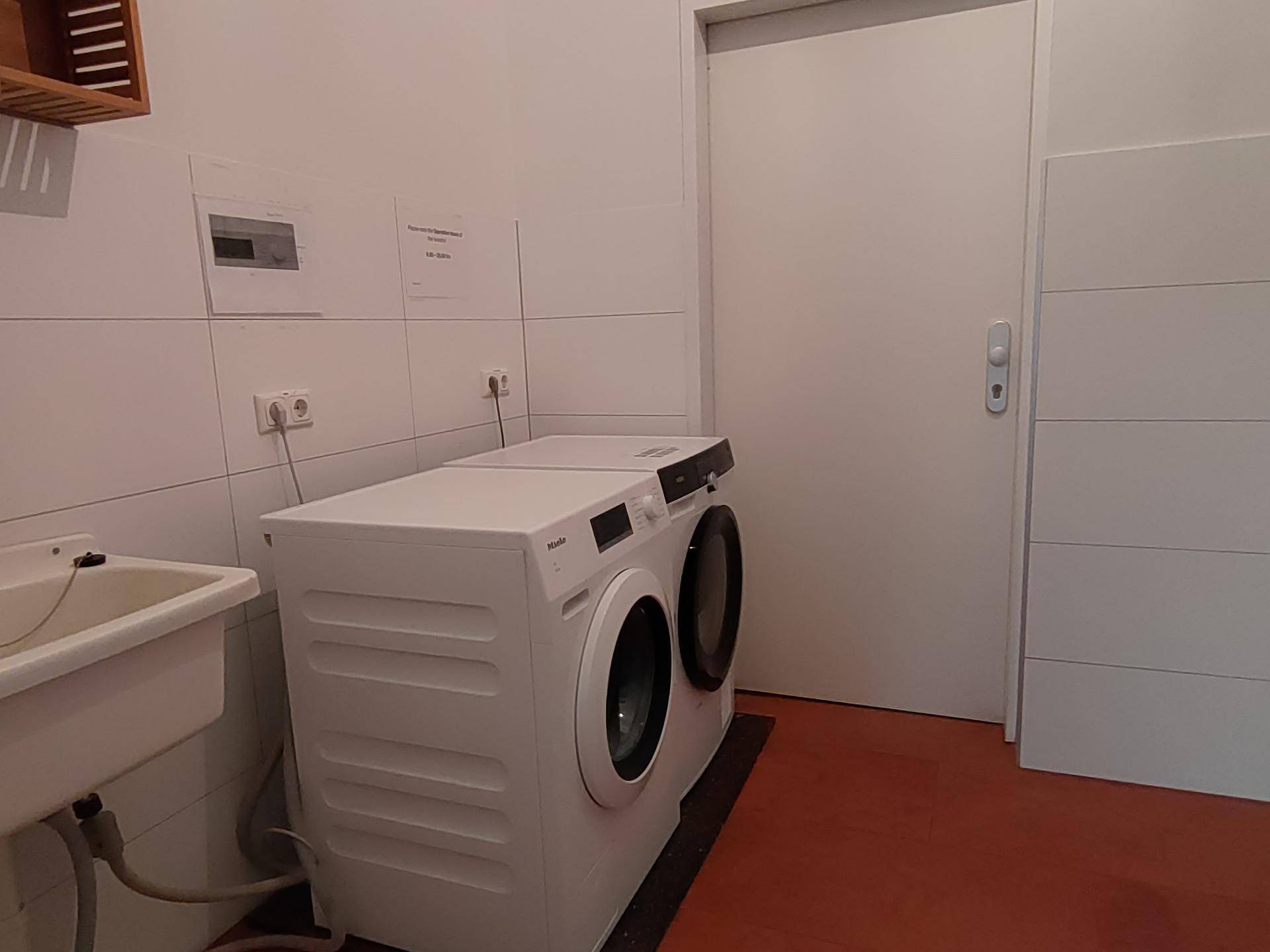 Waschküche mit Waschmaschine, Waschbecken und praktischen Ablagemöglichkeiten.