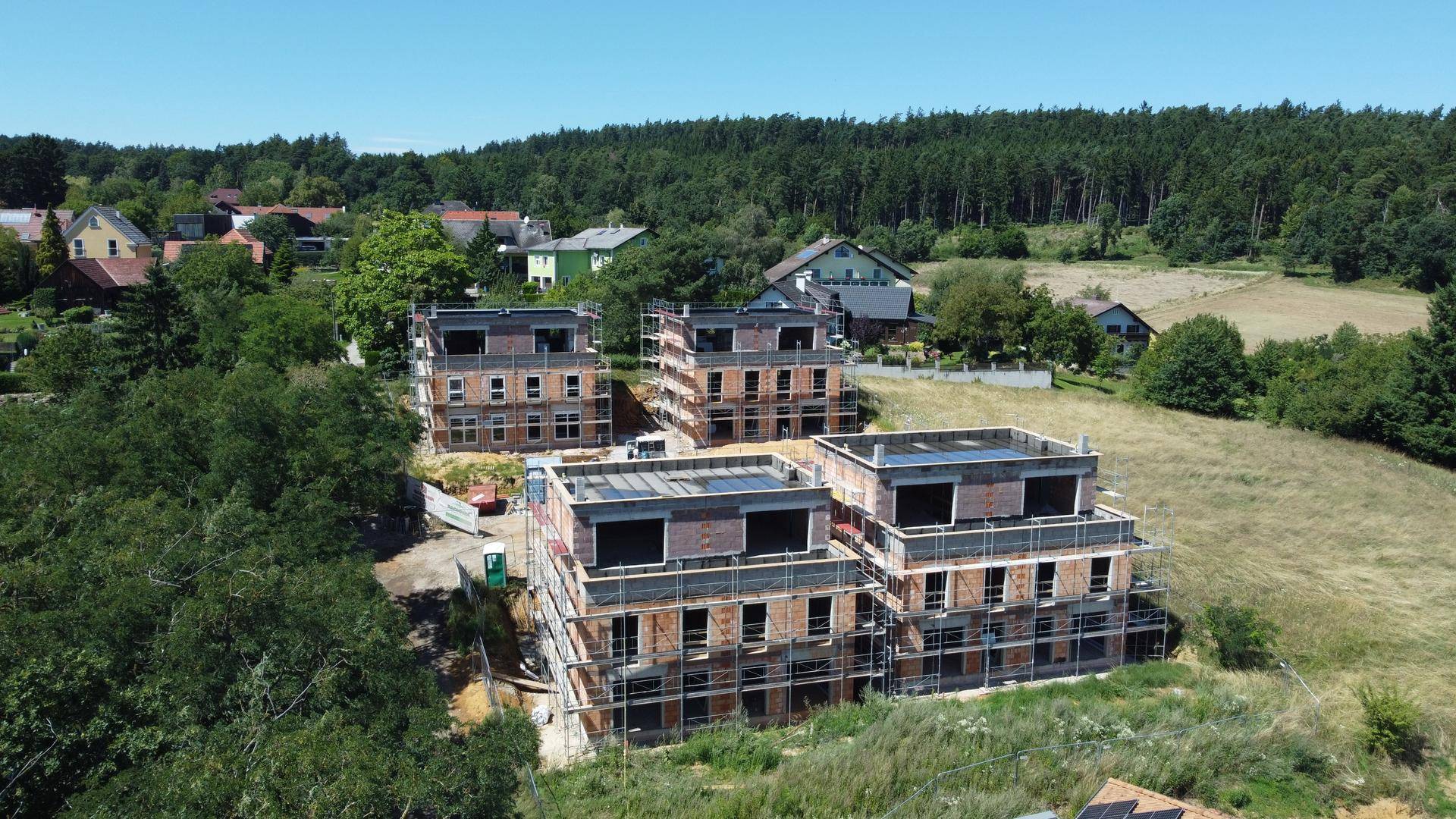 Baustelle von Reihenhäusern im Rohbauzustand mit Gerüsten, umgeben von Wald und Wiesen.