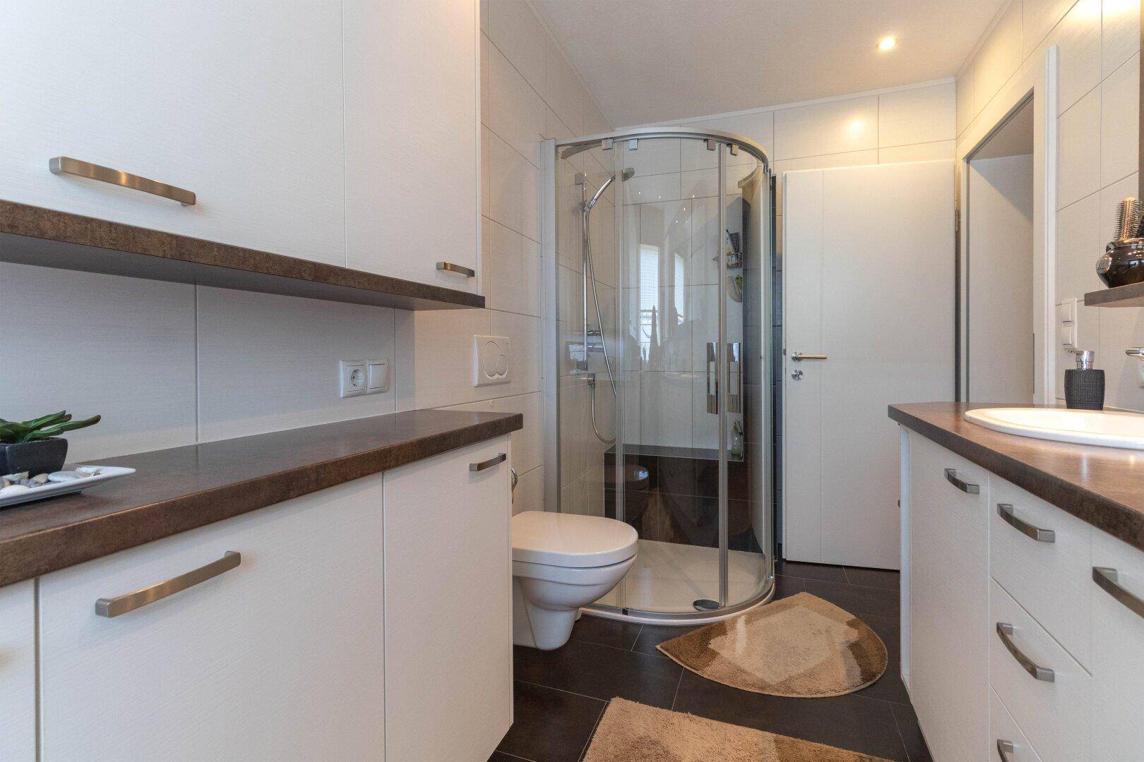Modernes Badezimmer mit Duschkabine, WC und weißen Schränken.