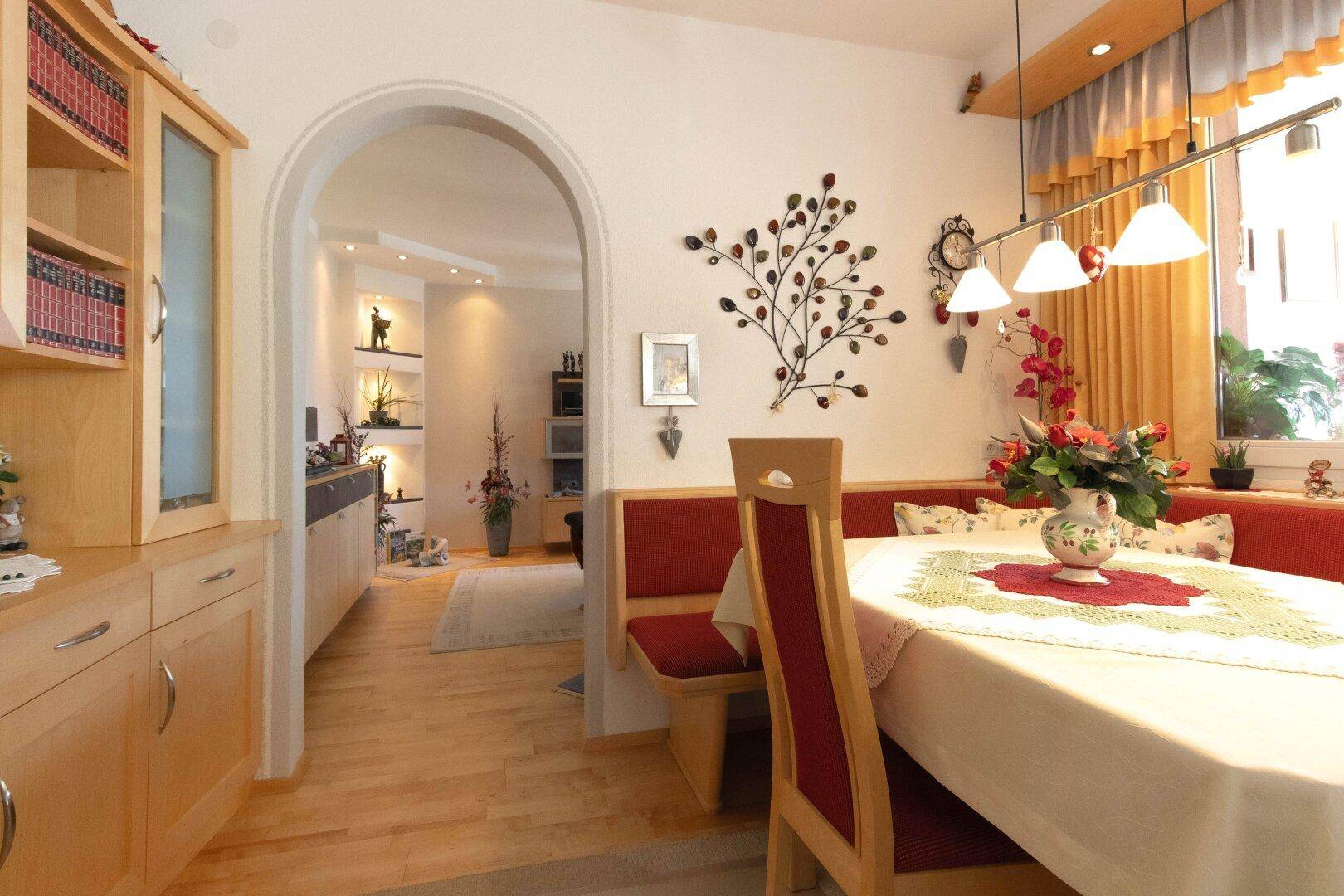 Essbereich mit Holztisch, roter Eckbank und Durchgang zum Wohnzimmer.