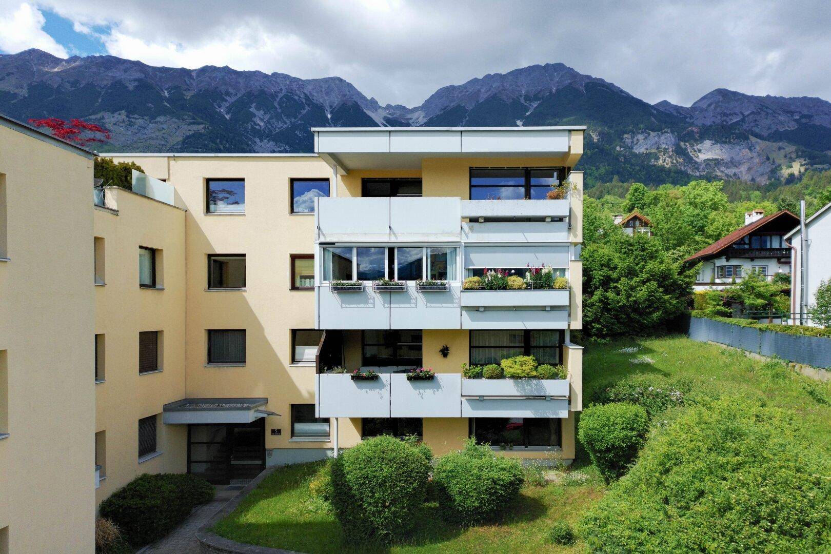 Modernes Mehrfamilienhaus mit Balkonen und beeindruckendem Bergblick im Hintergrund.